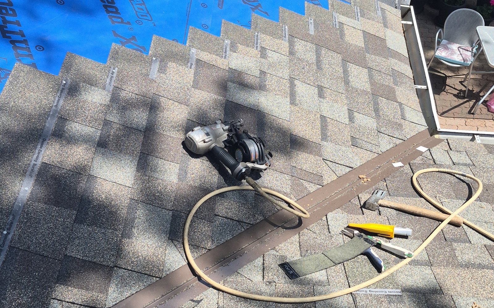 Shingle installation in progress beside blue underlayment and roofing tools