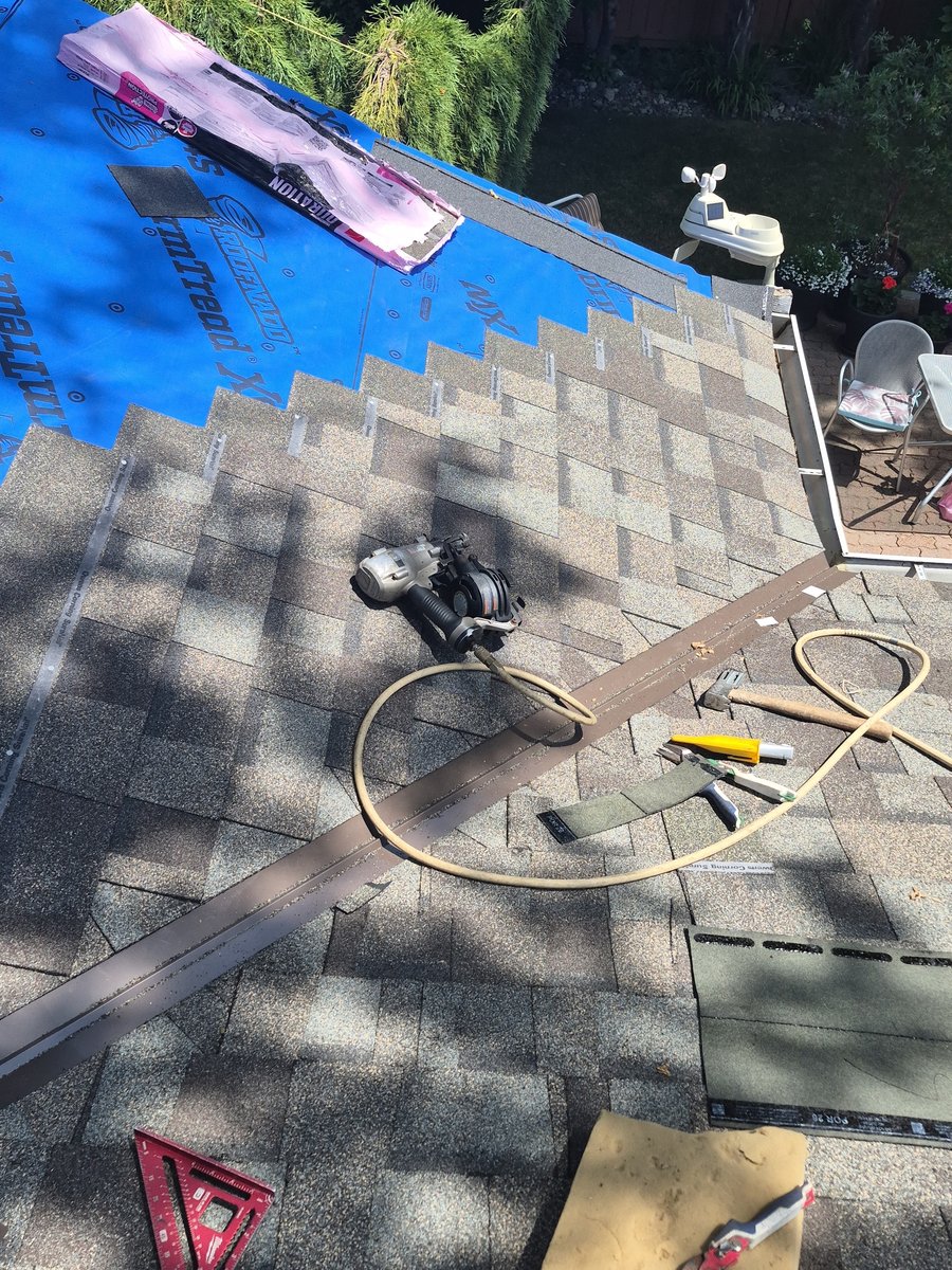 Roofing tools on shingles beside blue underlayment