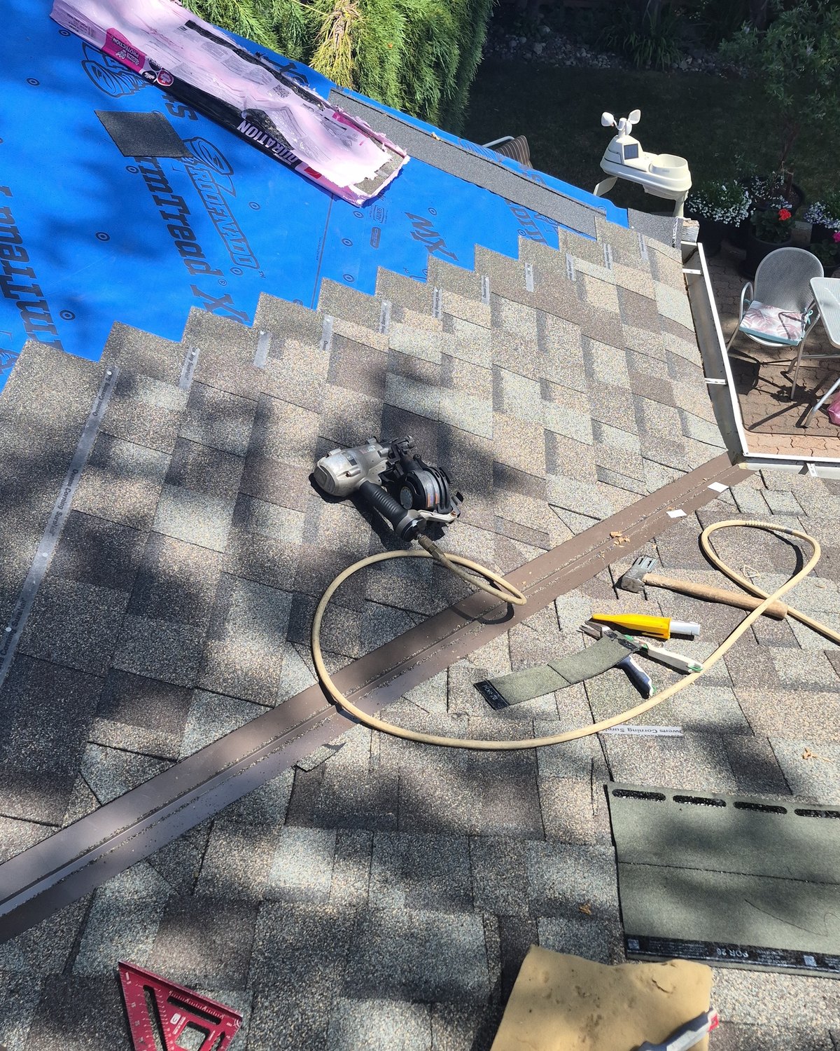 Roofing tools and partially laid shingles beside blue underlayment